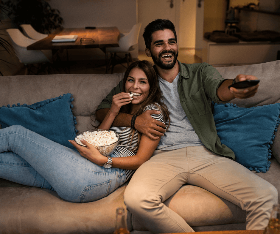 young couple watching virtual date night with popcorn in living room